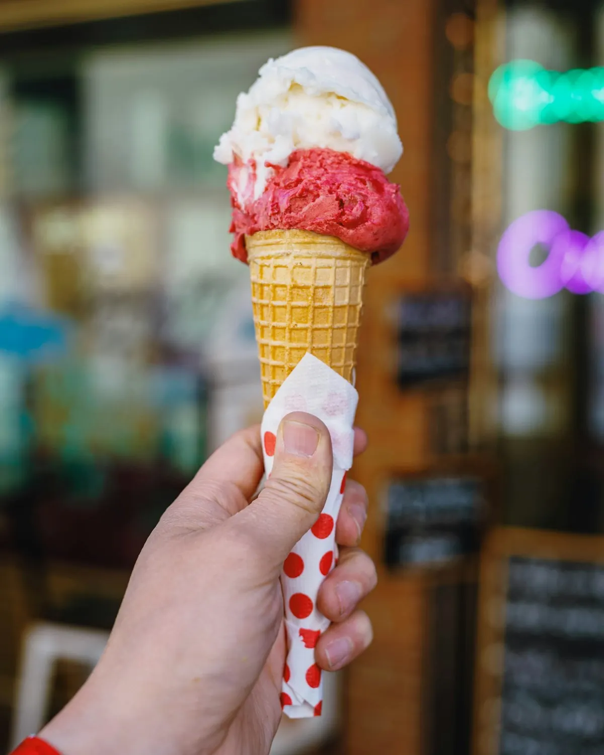 Casquinha com sorvete de morango e creme segurada na frente da vitrine